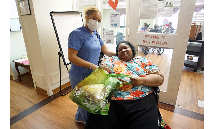 Extended Care Adopt-a-Resident Day 5-11-2022 Female employee giving reusable bag to woman for web