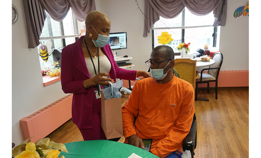 Extended Care Adopt-a-Resident Day 5-15-2025 Veronica Onwunaka handing present to man in orange for web